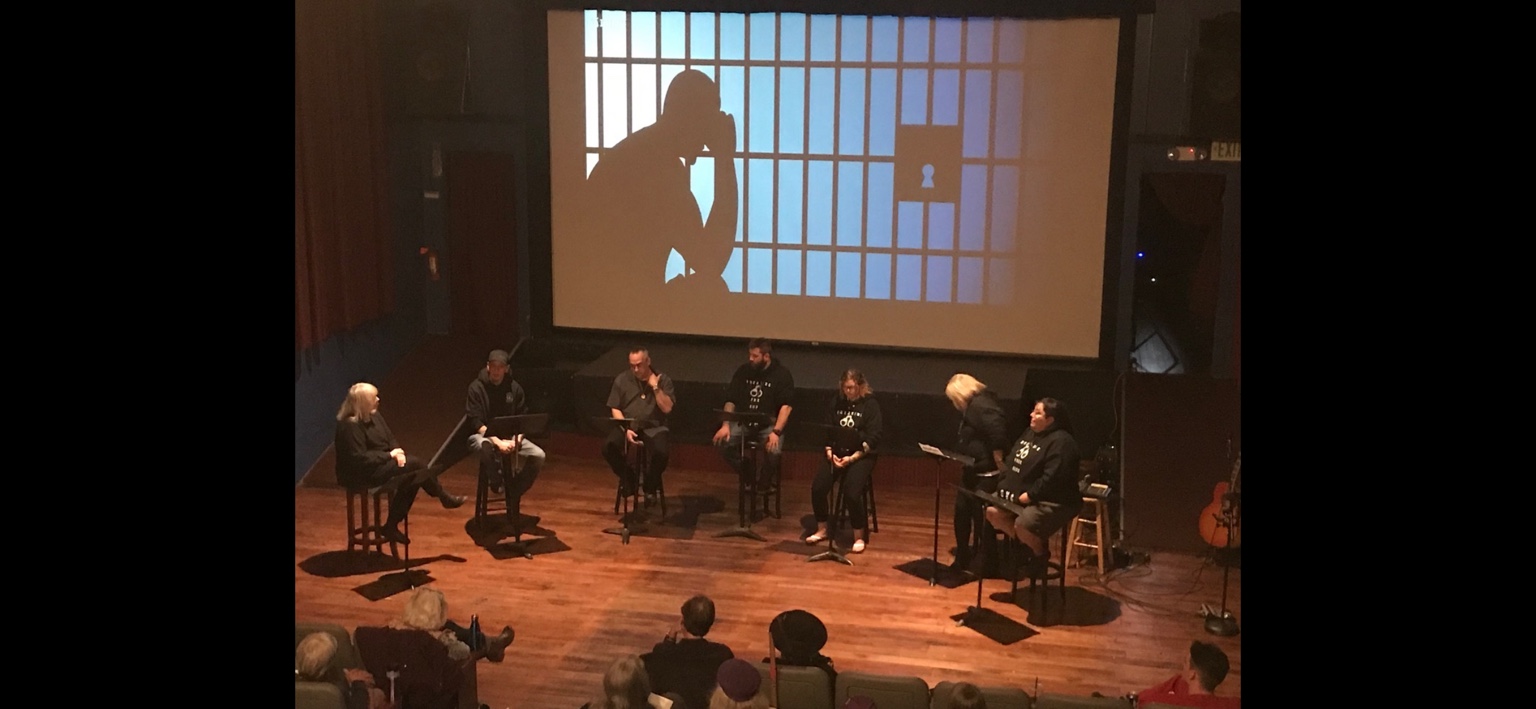 Seven TASA performers seated in a semicircle during a reader's theatre performance